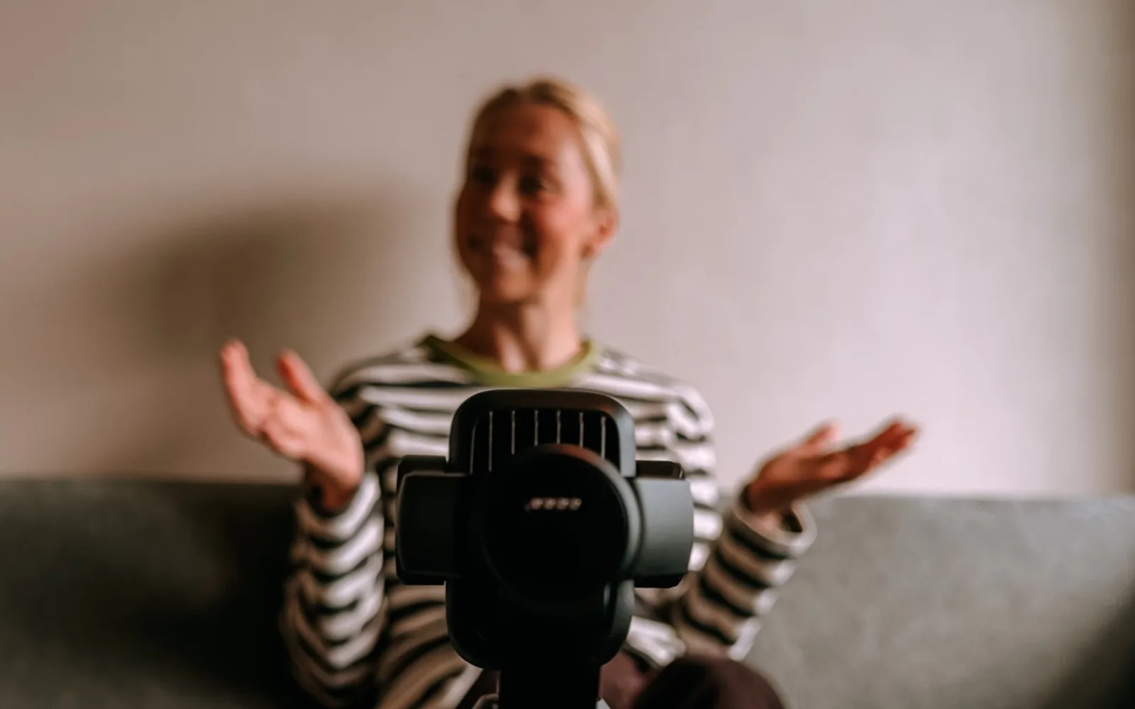 Veronica Undseth sitter i en sofa og snakker med hendene mens et lite kamera på stativ i forgrunnen filmer henne.
