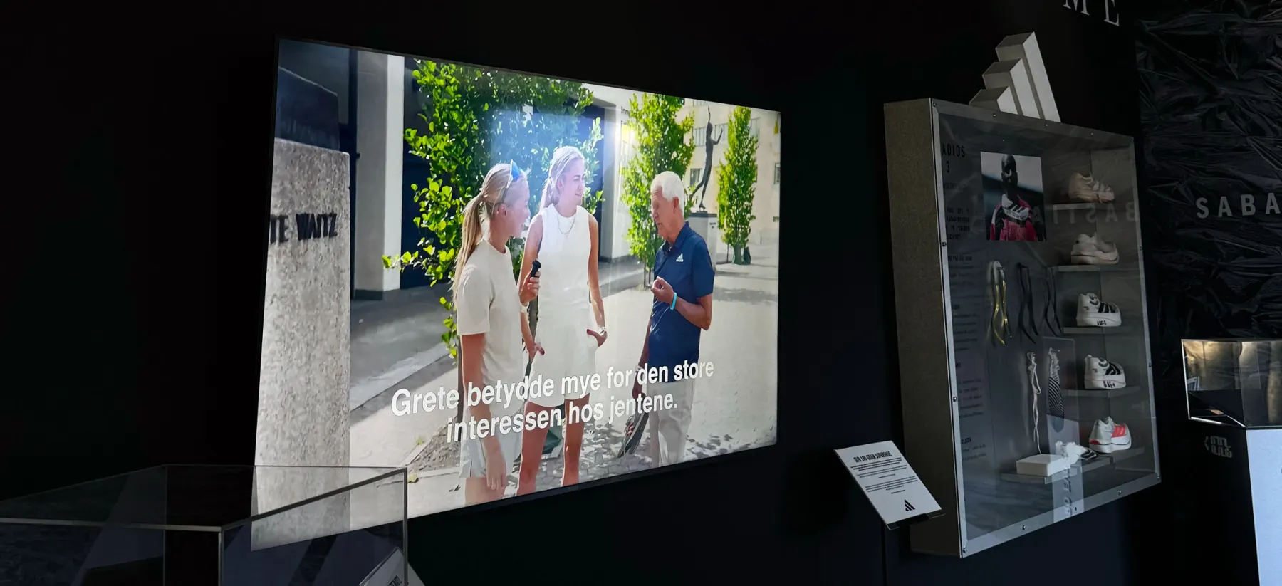 Storskjermen i historiehjørnet på expoen viser Grete Waitz-filmen med Jack Waitz, Veronica Undseth og Amalie Sæten, ved siden av montrene med skoene
